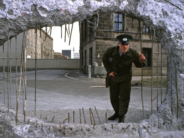 An East German border guard looks through a hole in the wall towards West Berlin. 14 Nov 1989