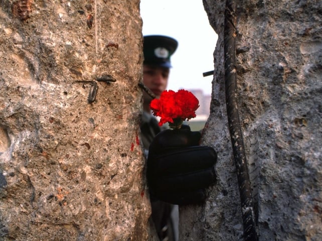 An East German border guard offers a flower through a gap in the Berlin Wall. 10 Nov 1989