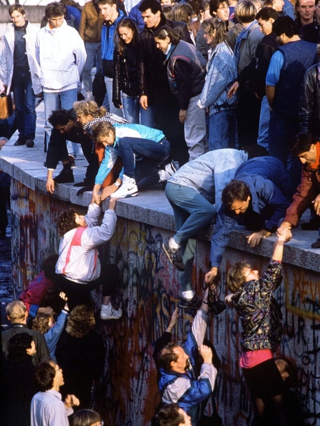 Hundreds of rejoicing Berliners help each other get to either side of the Berlin Wall. On November 9, the border separating East and West Germany was officially opened causing the 'fall of the Berlin Wall' and symoblising the end of the 'Cold War'