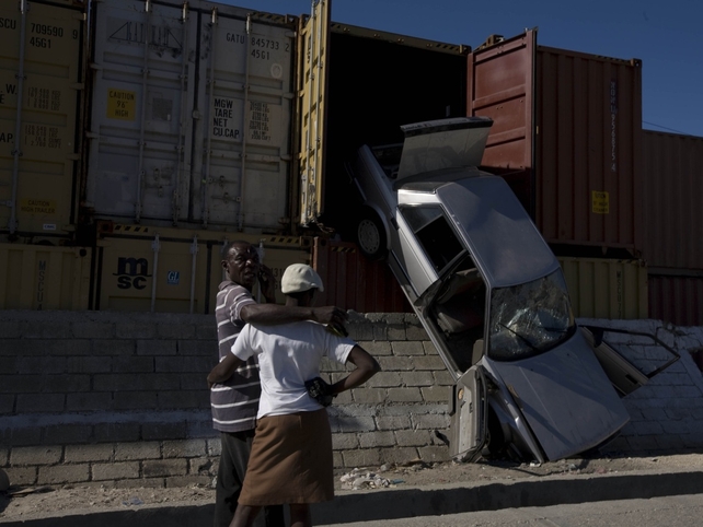 Earthquake survivors stand on the street near a car that has fallen out of a cargo container