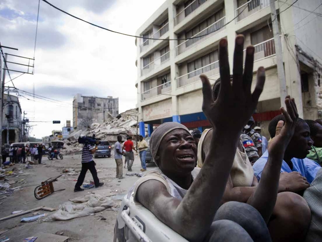 A man cries as he rides on a truck travelling past collapsed buildings in Petionville