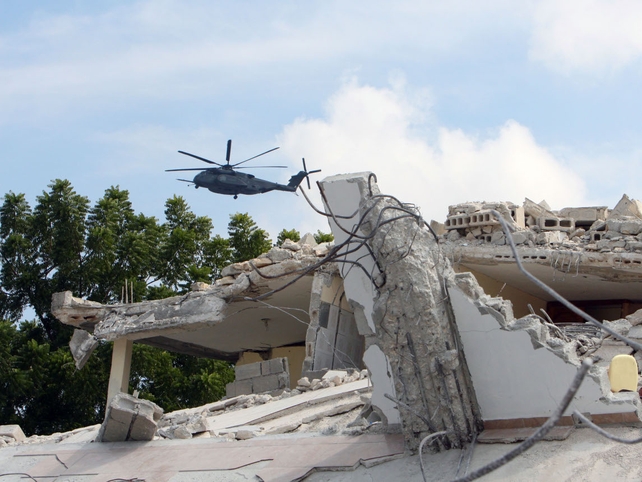 A military helicopter flies past the rubble of a collapsed school