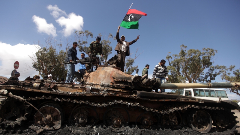 Libyan rebels wave their flag on top of a wrecked tank belonging to Gaddafi's forces outside Benghazi