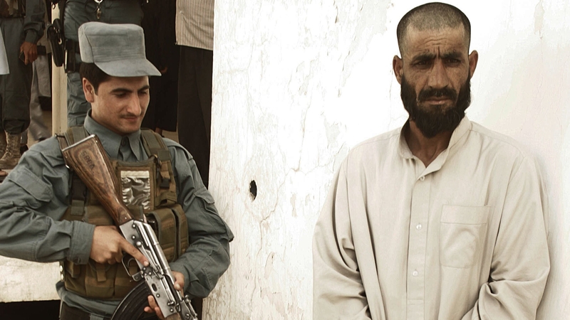 Afghanistan - An Afghan policeman stands guard next to an arrested Taliban commander suspect in Herat city yesterday