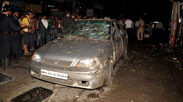 Mumbai - Indian bystanders gather around a damaged vehicle at a bomb blast site