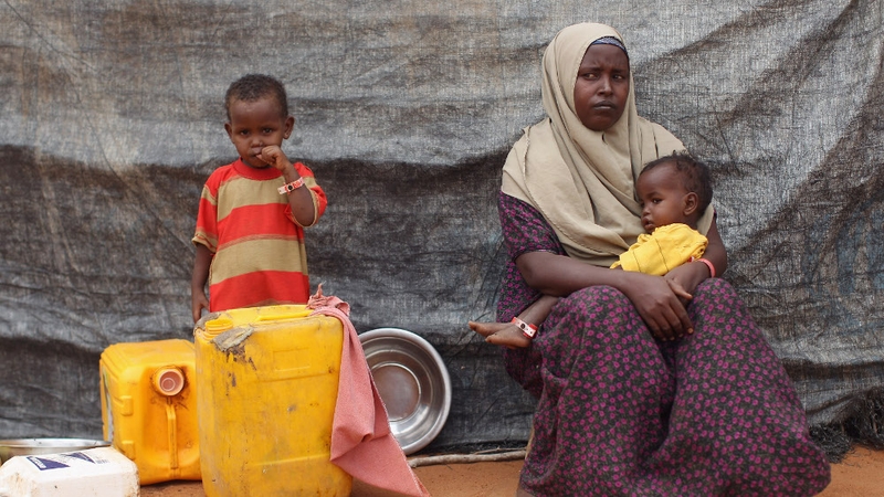 Kenya - Newly arrived Somali refugees sit outside a hut on the edge of the Hagadera refugee camp