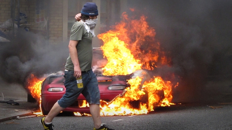 A man walks past a burning car in Hackney