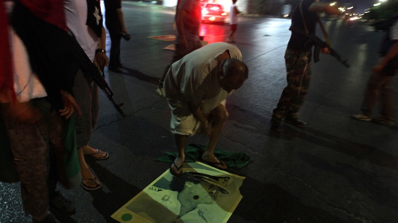 A man stands on a picture of Muammar Gaddafi