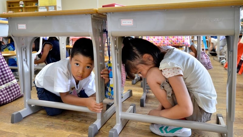 Elementary school children take cover under their desks as part of the nationwide earthquake drill
