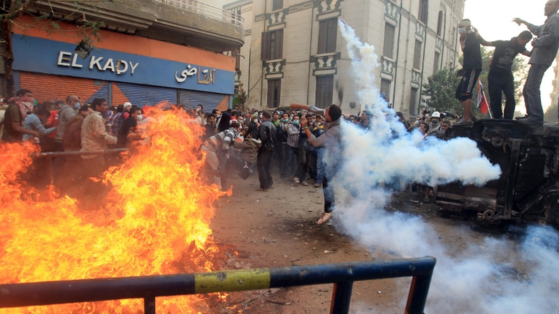 A protester throws a tear gas canister on the third day of clashes with police at Tahrir Square