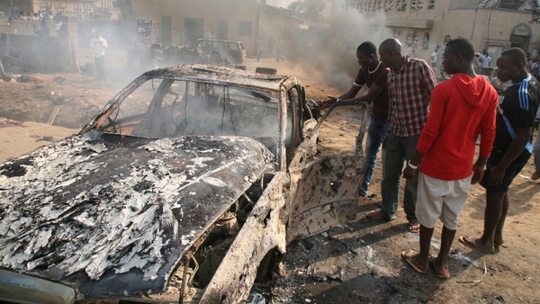 Men look at the wreckage of a car following a bomb blast at St Theresa Catholic Church