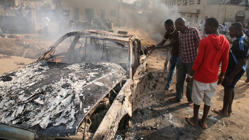 Men look at the wreckage of a car following a bomb blast at St Theresa Catholic Church