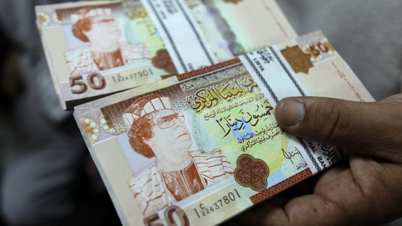 A banker shows 50 Libyan Dinar bank notes bearing the image of ousted leader Moamer Gadaffi