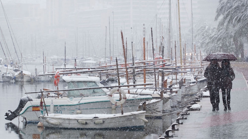 A couple walks near boats during a snowfall in Palma de Mallorca in the Balearic Islands