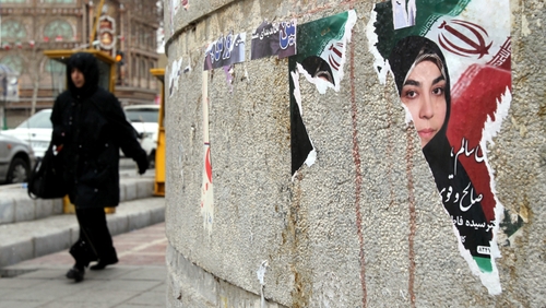 An Iranian woman walks past a torn electoral poster for a parliamentary candidate a day after the elections in Tehran