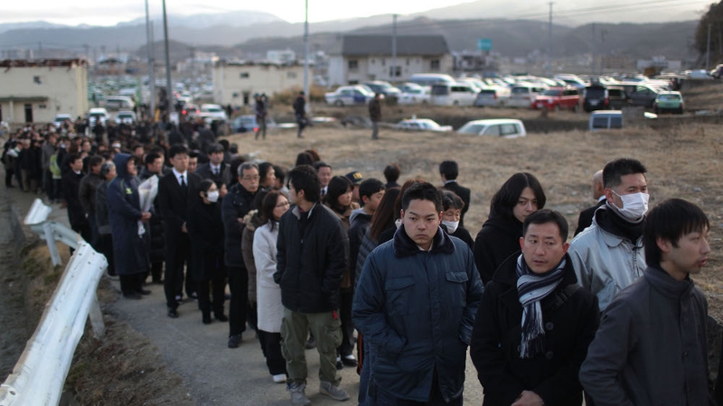 Long lines of people wait to place a flower at the Rikuzentakata City memorial ceremony