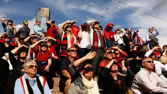 Fans shield their eyes as they watch the televised broadcast of the service