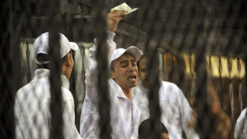 One of the defendants shouts as he holds up a Koran behind a cage in the court room in Cairo
