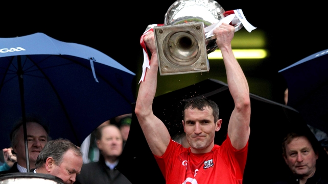 Cork captain Graham Canty celebrates with the Division 1 cup as Taoiseach Enda Kenny looks on, blue from the cold and perhaps a little green with envy as his native county Mayo were beaten
