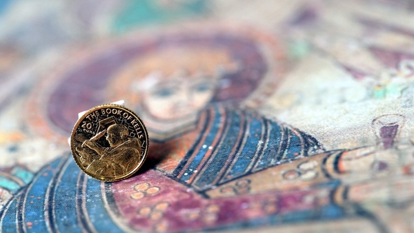 The coin depicts a monk working on The Book of Kells