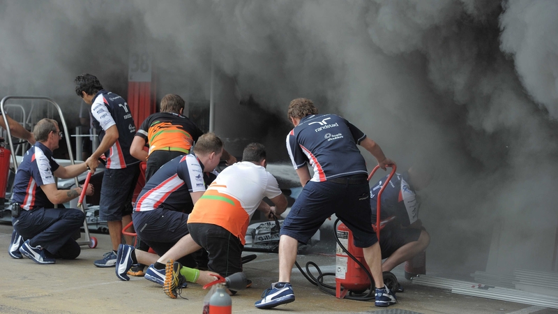 Racing team crews try to extinguish the fire in the Williams racing pit