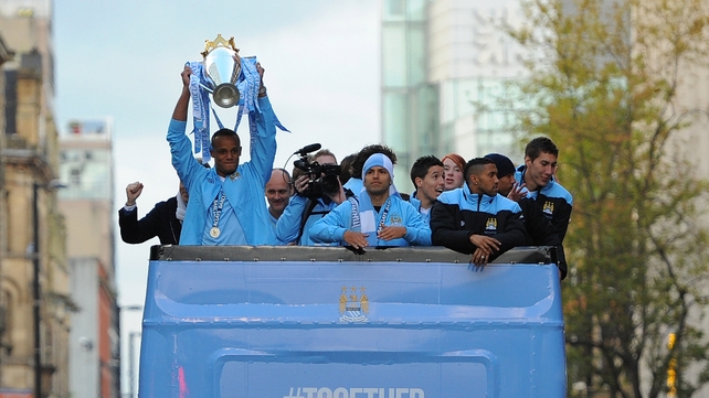 Manchester City's Vincent Kompany raises the trophy as he stands with teammates on an open-topped bus after becoming English Premier League champions after a 44-year wait