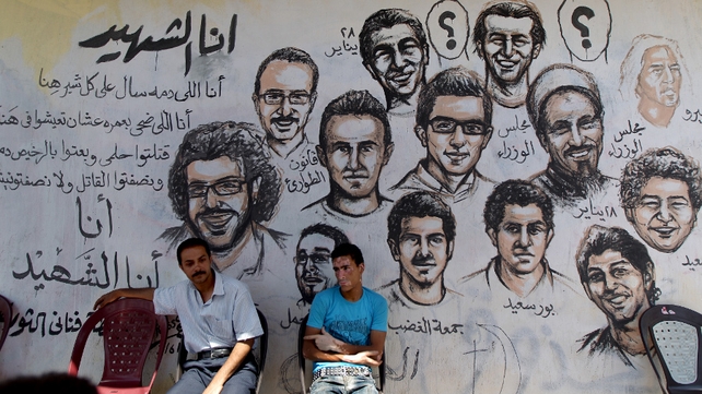 Egyptians sit in front of a mural picturing those killed during the revolution, days before second round voting