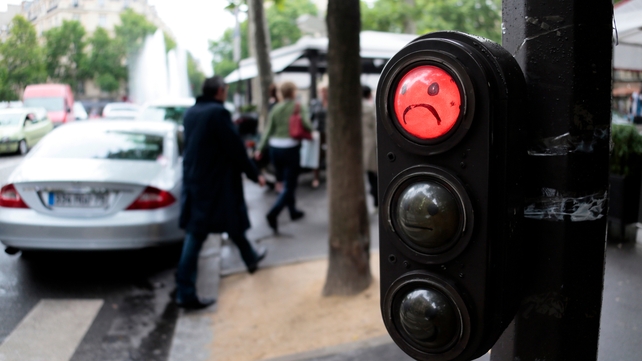 Graffitti depicting a sad face on a red traffic light in Paris