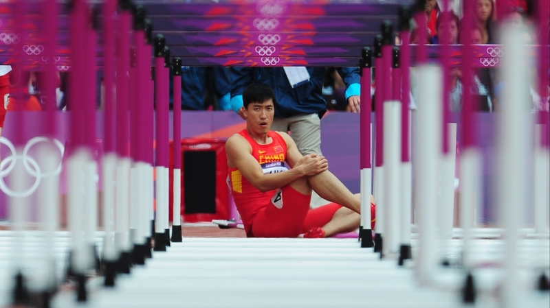 Xiang Liu of China sits on the track after getting injured