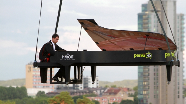 A stuntman pretends to play the piano as he and his cardboard instrument are lifted by a hot air balloon over Vilnius, Lithuania