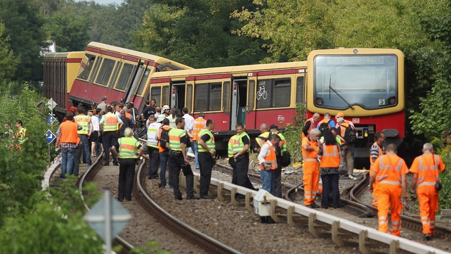 Police, firemen and emergency rescue workers stand around the wreckage of a derailed S-Bahn commuter train in Berlin
