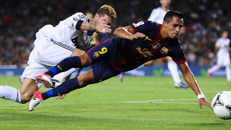 Alexis Sanchez of Barcelona is brought down by Sergio Ramos
