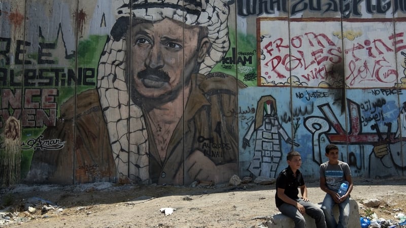 A Palestinian boys sit next to a mural of late Palestinian leader Yasser Arafat