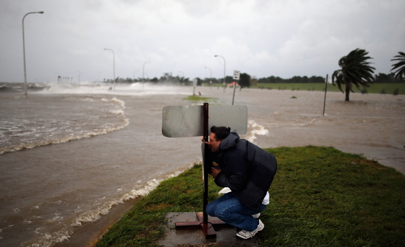 A man crouches behind a sign to avoid the high winds on the lake