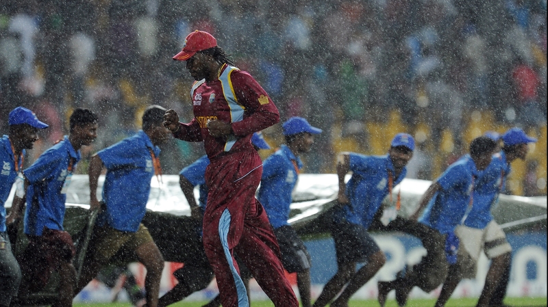 West Indies batsman Chris Gayle runs for cover as ground staff pull a tarp over the pitch as rain stops play