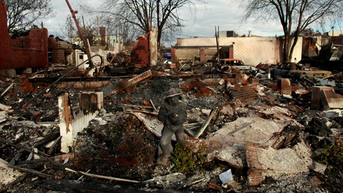 A statue of a firefighter remains in front of a burnt house in Queens