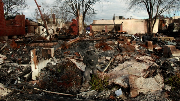 A statue of a firefighter remains in front of a burnt house in Queens