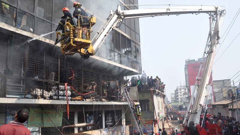 Bangladeshi firefighters use a water cannon on a crane to try to control the fire