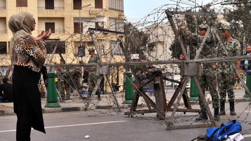 An Egyptian woman prays in front of Egyptian security as they lay out barbed wire along streets leading to the presidential palace