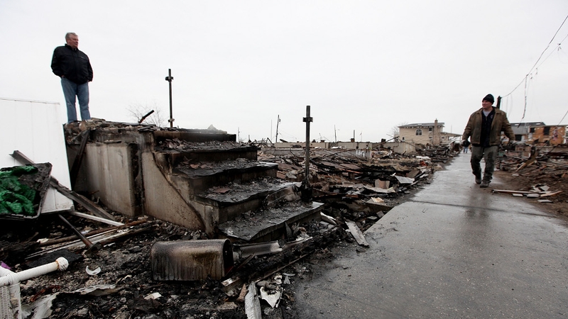 Dennis Kane (l) stands above the charred remains of his destroyed home in the hard hit Breezy Point neighbourhood of Queens in New York City