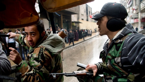 Two rebel fighters crouch on the back of their machine gun mounted pick up truck as they approach an exposed intersection in an Aleppo neighbourhood