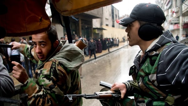Two rebel fighters crouch on the back of their machine gun mounted pick up truck as they approach an exposed intersection in an Aleppo neighbourhood