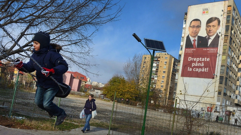A girl surges on a swing as a poster of the Social Liberal Union (USL) party is displayed, Victor Ponta (l) and National Liberal Party leader Crin Antonescu (r) on a block of flats in Bucharest