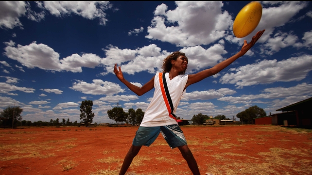A boy catches an Australian rules football as the Indigenous All Stars visit Yuendumu School in the Australian outback
