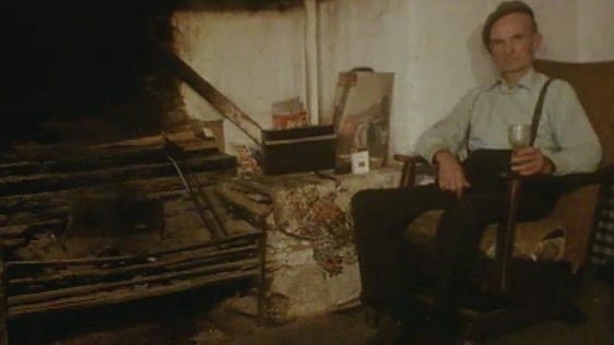 An old man sits in an armchair by a large hearth.