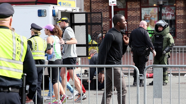 Members of the bomb squad investigate a suspicious item on the road as runners pass near Kenmore Square
