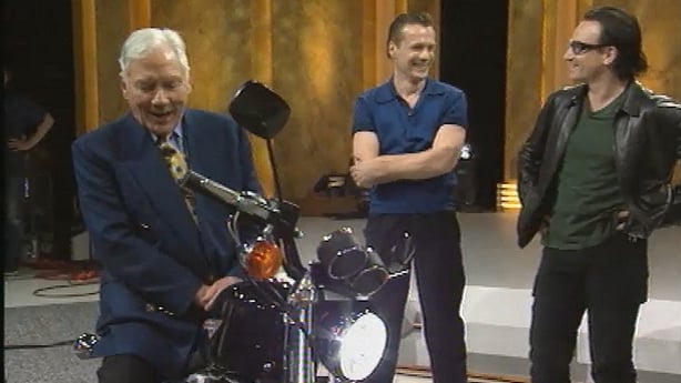 Gay Byrne marvels at a Harley Davidson motor bike as U2 look on