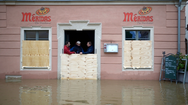 Three men stand behind wooden panels erected to protect a restaurant against the floods of the river Elbe in Pirna, eastern Germany