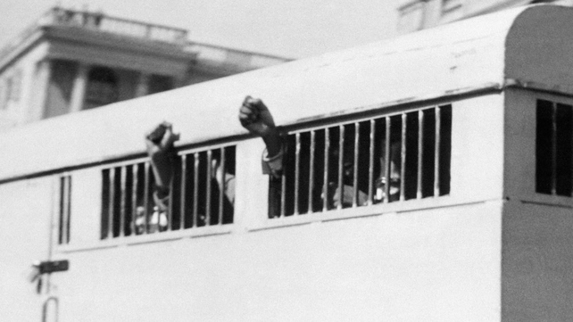 Nelson Mandela is among eight men sentenced to life in prison in June 1964. Some raise their fists in defiance through the barred windows of a prison car