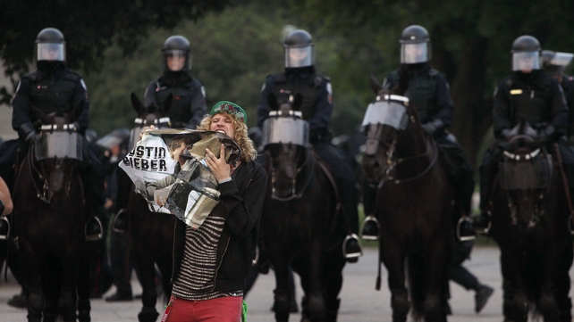 A protester destroys a poster of Justin Bieber as mounted riot police look on in Toronto, Canada in 2010